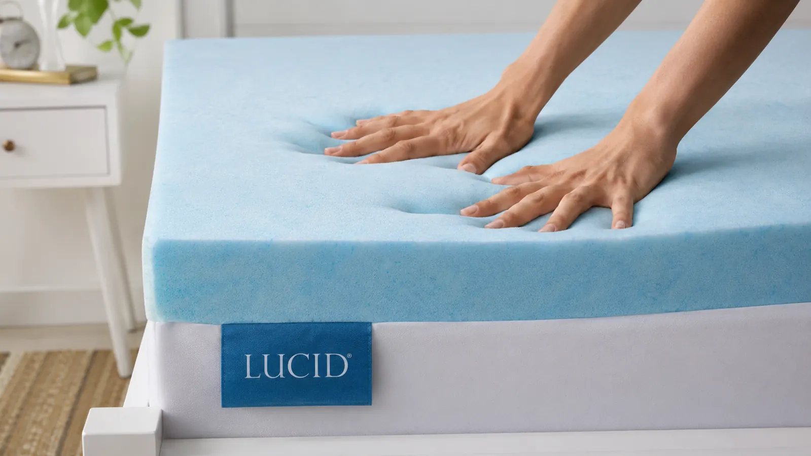 Close-up of a hand pressing into the surface of a gel memory foam mattress topper, showing the foam conforming around the hand