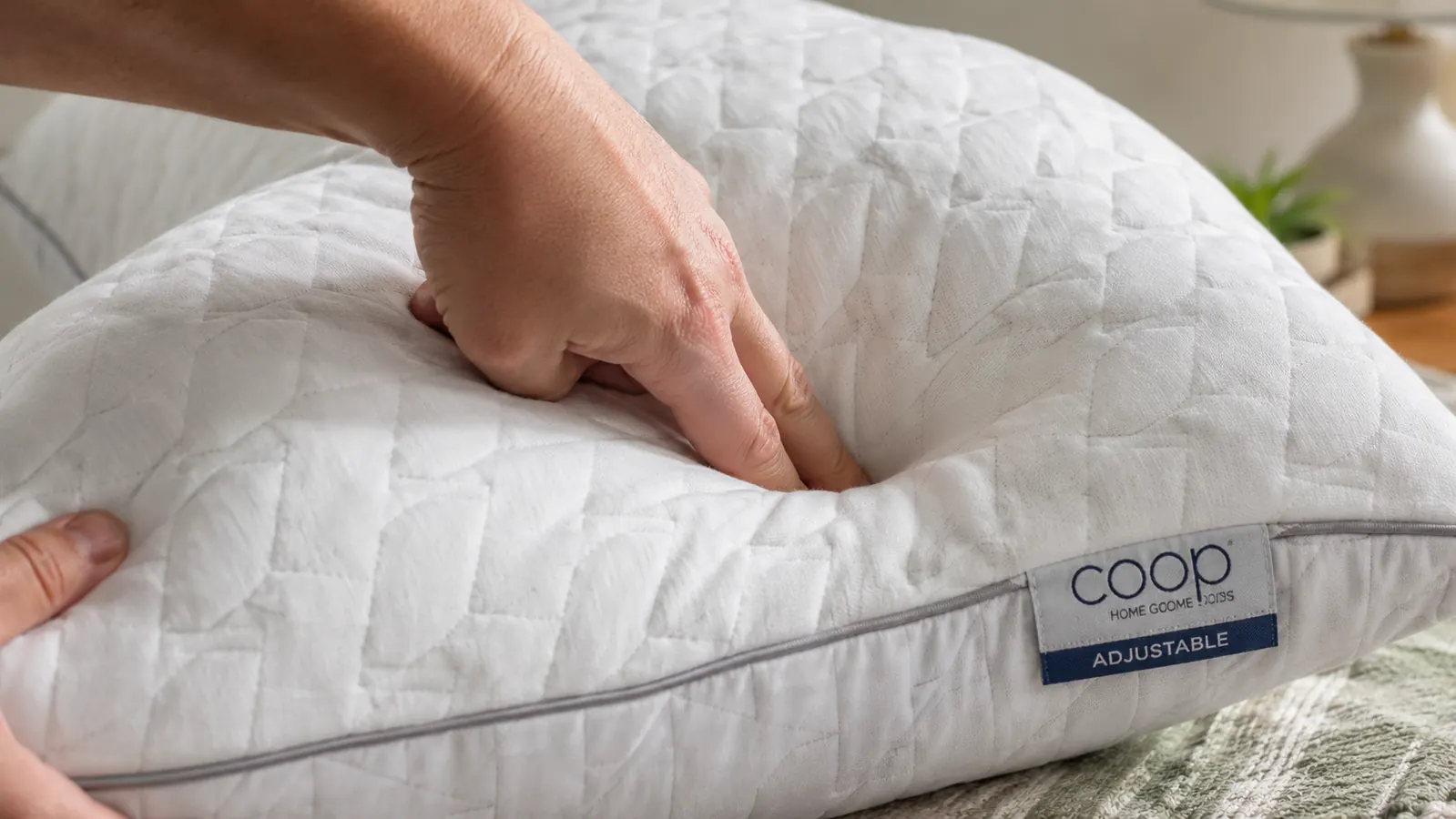 A hand pressing two fingers firmly into the center of the Coop Crescent pillow to show slow rebound of compressed shredded foam
