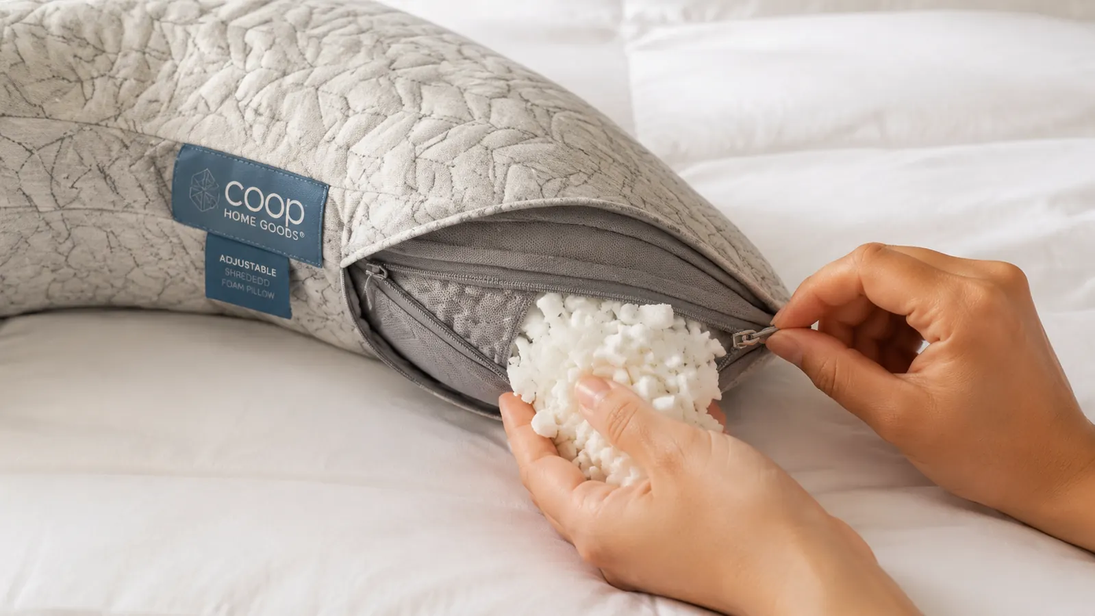 Close-up of hands unzipping the Coop Crescent pillow's inner zipper to remove a handful of shredded foam fill
