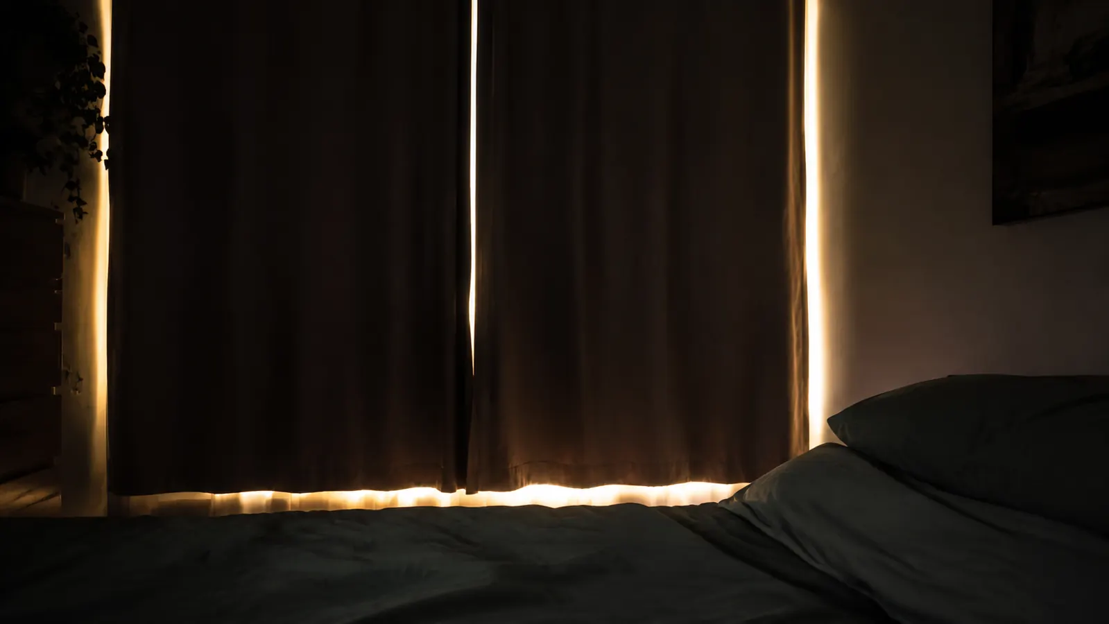 Bedroom window at dawn with light seeping around curtain edges, illustrating the light-leak problem a sleep mask addresses